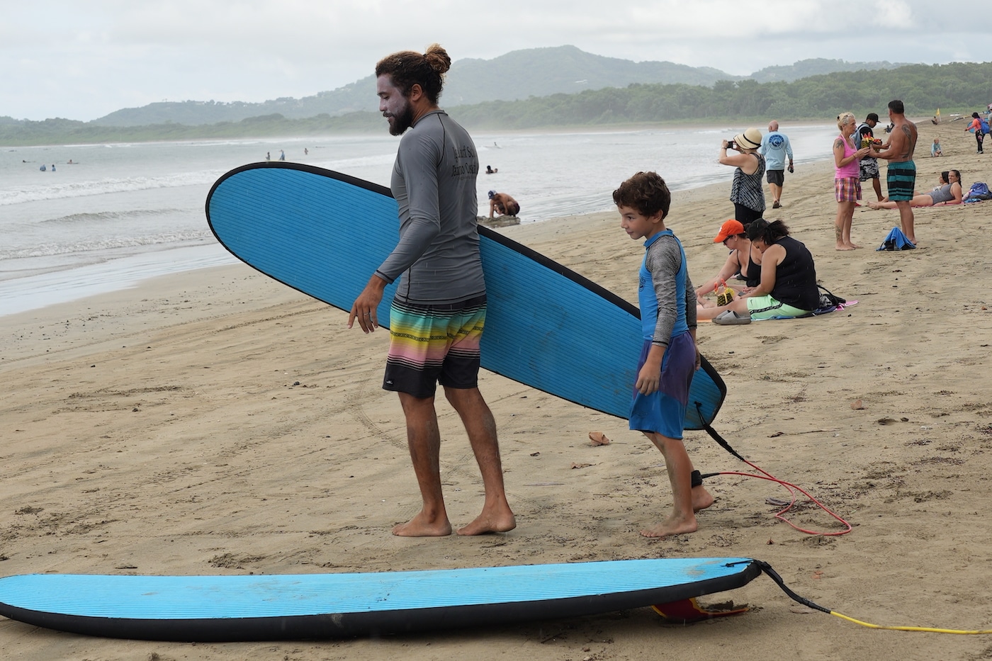 Iguana Surf - A man and a young boy holding a surf board walking towards the ocean. 
