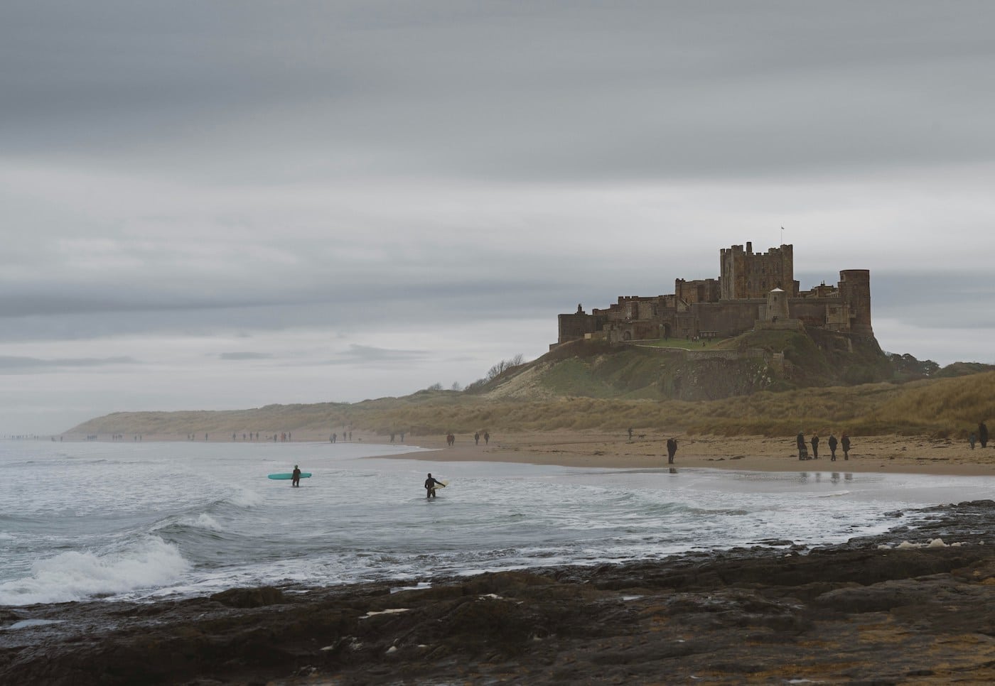 Bamburgh Castle with surfers in the sea in the foreground