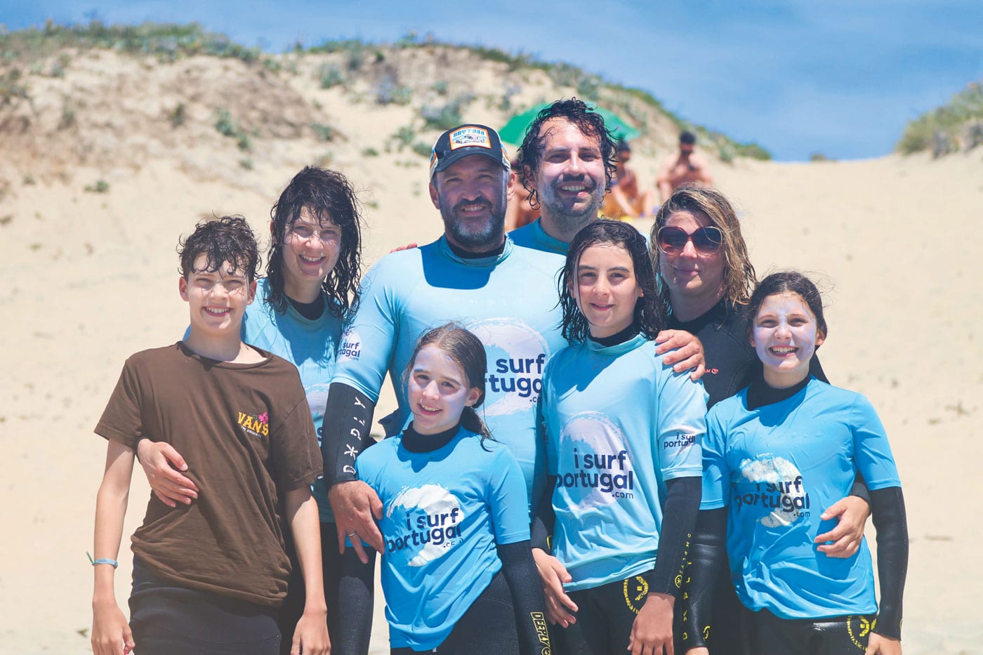 A family posing for a photo together after a surf session in front of the sand dunes.