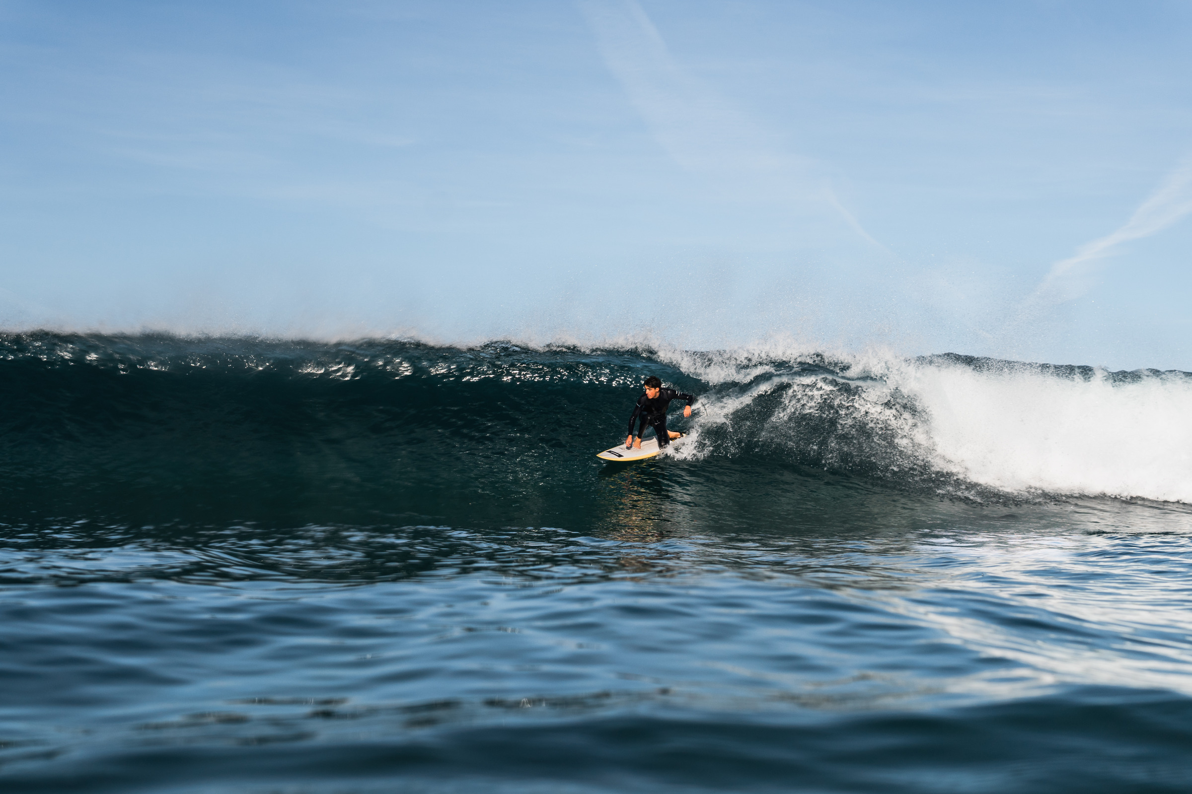 Surfer crouched low in a dark wave as the lip throws