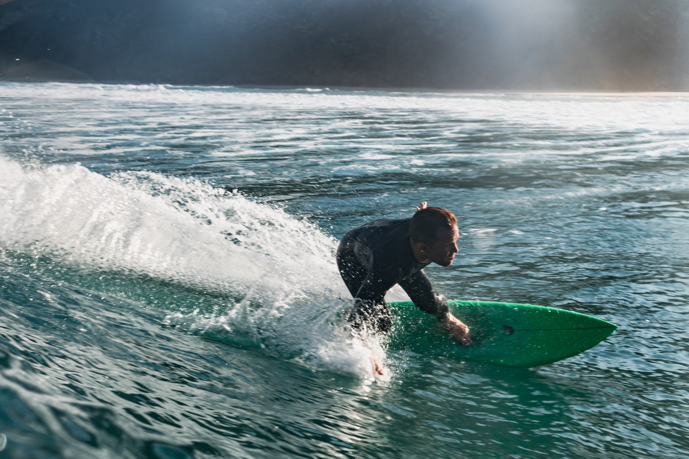 Surfer carving a turn on a green board with spray trailing behind