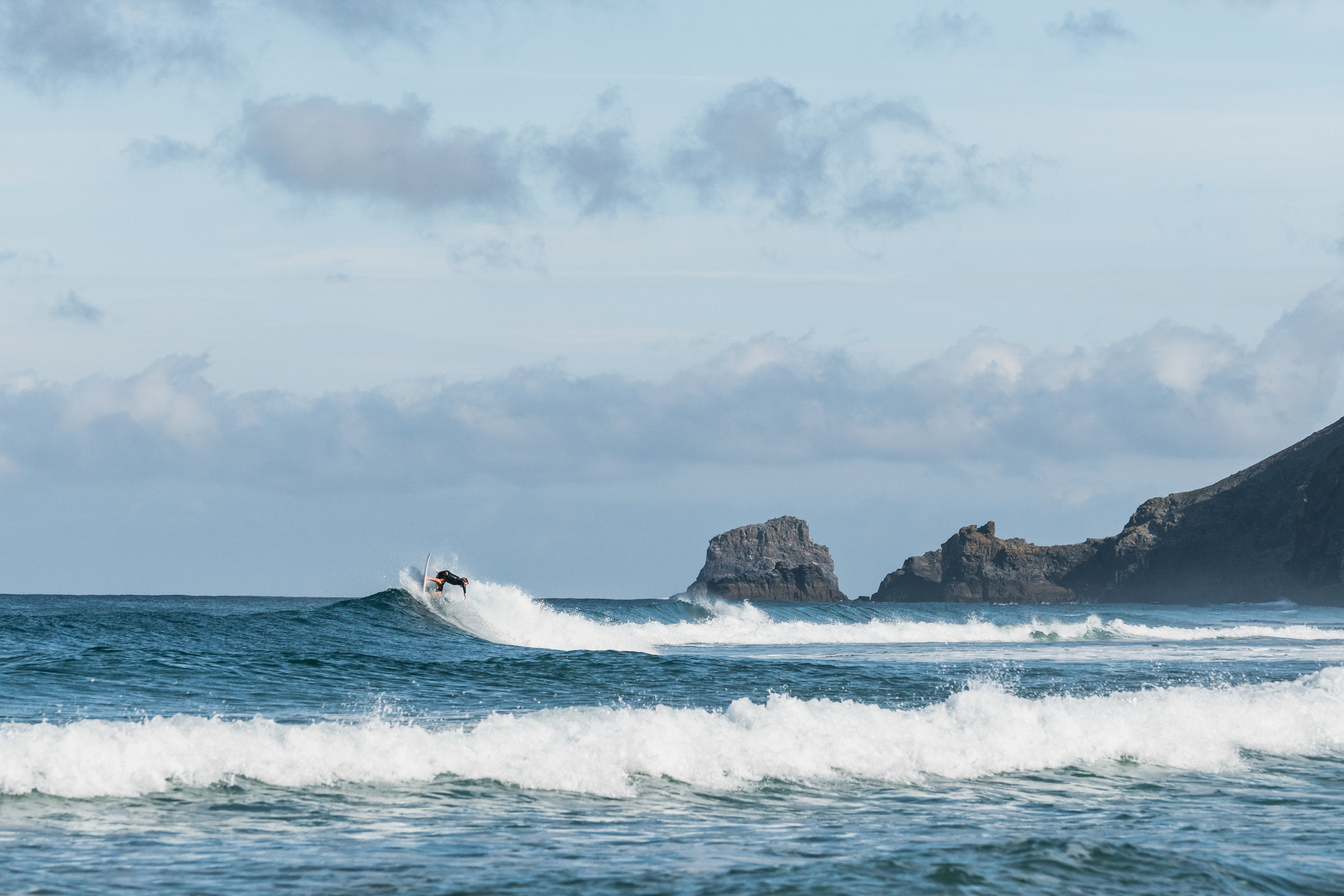 Surfer carving at the top of a small wave in front of rocks and a headland
