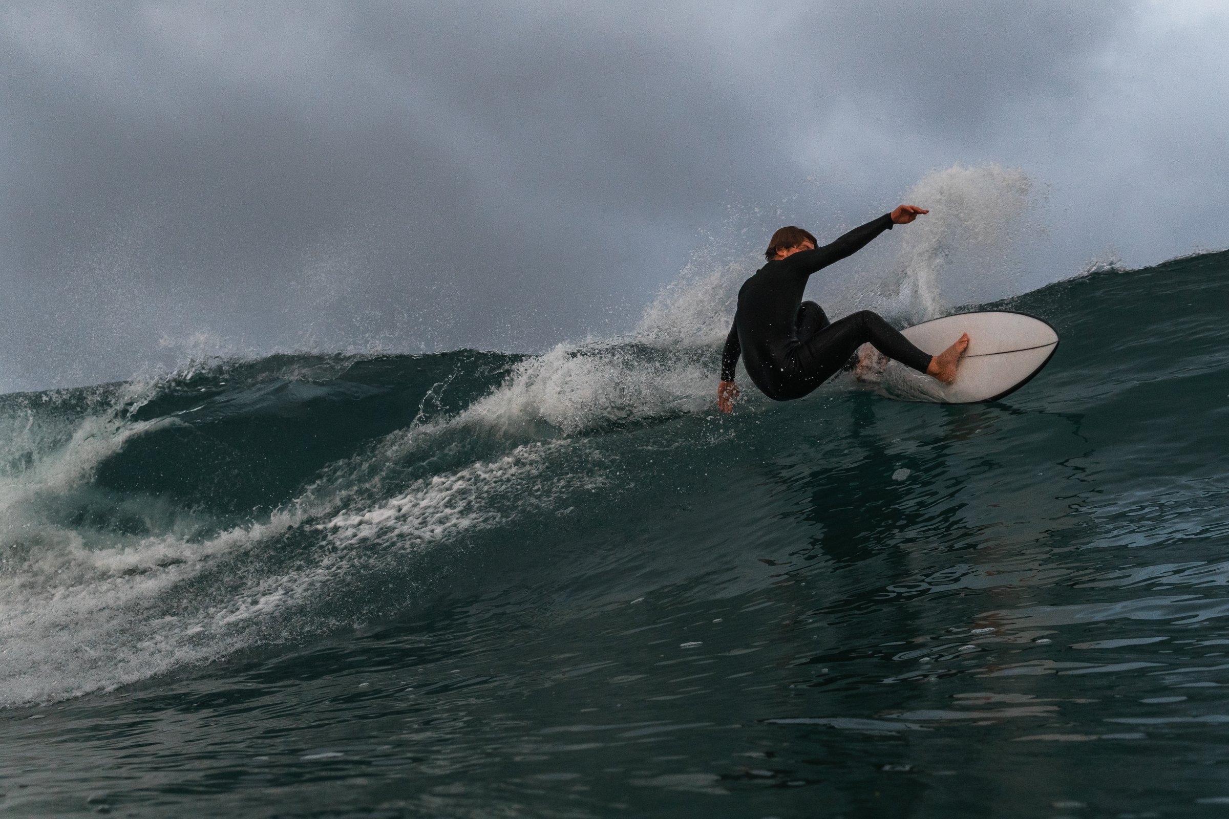 Finley Donovan carving a turn on a white board under a heavy grey sky