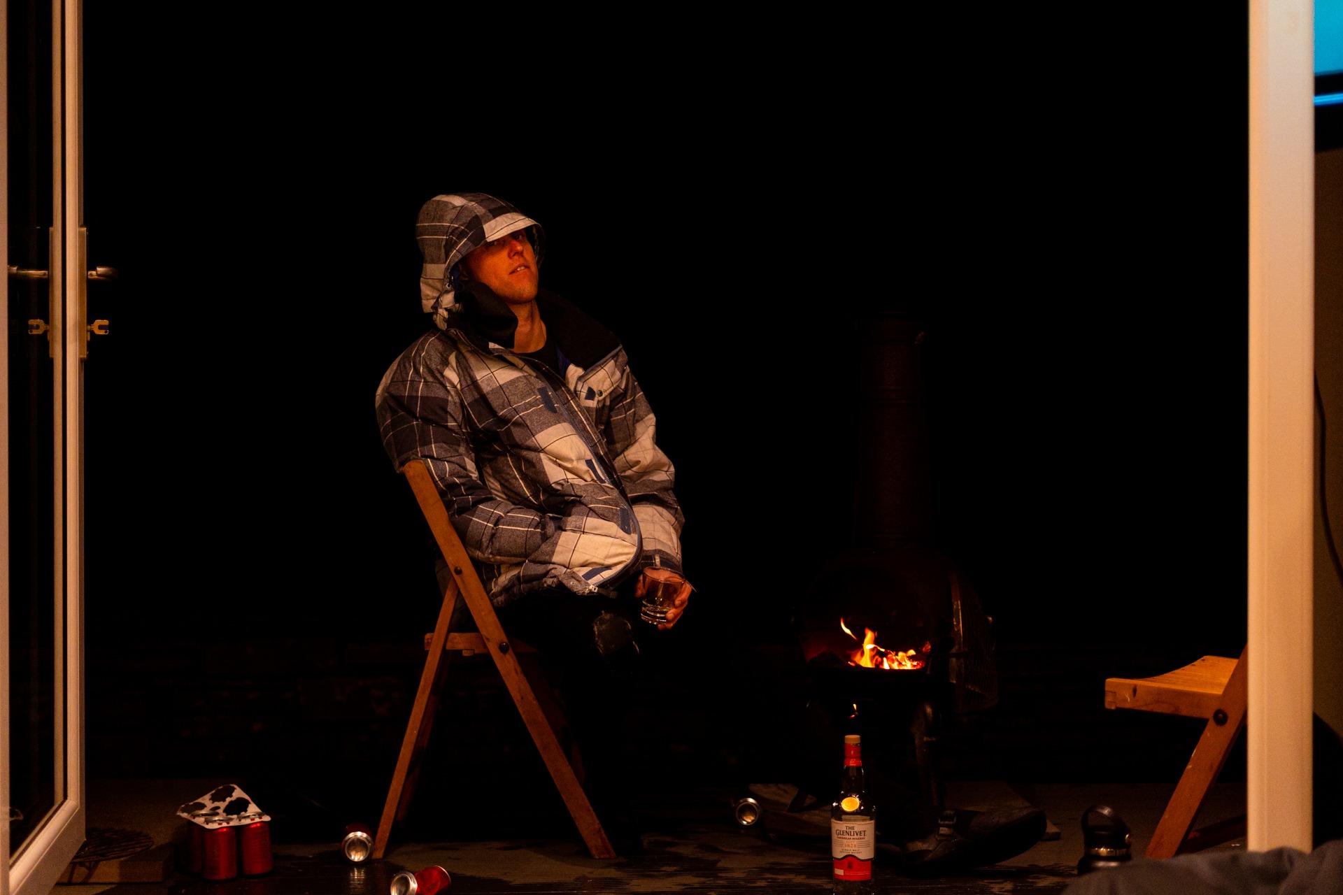 Mark Boyd sitting back in a folding chair by a small fire at night with a drink in his hand