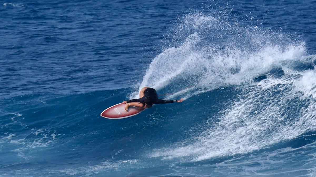 Frankie Harrer laid over on a red surfboard in a deep cutback, spray fanning across dark blue water