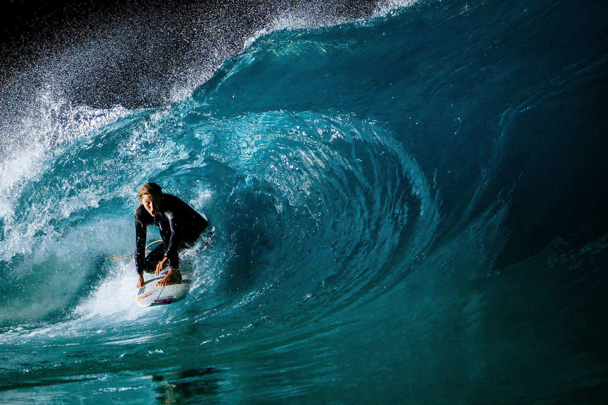 Surfer riding a deep blue barrel under floodlights at night