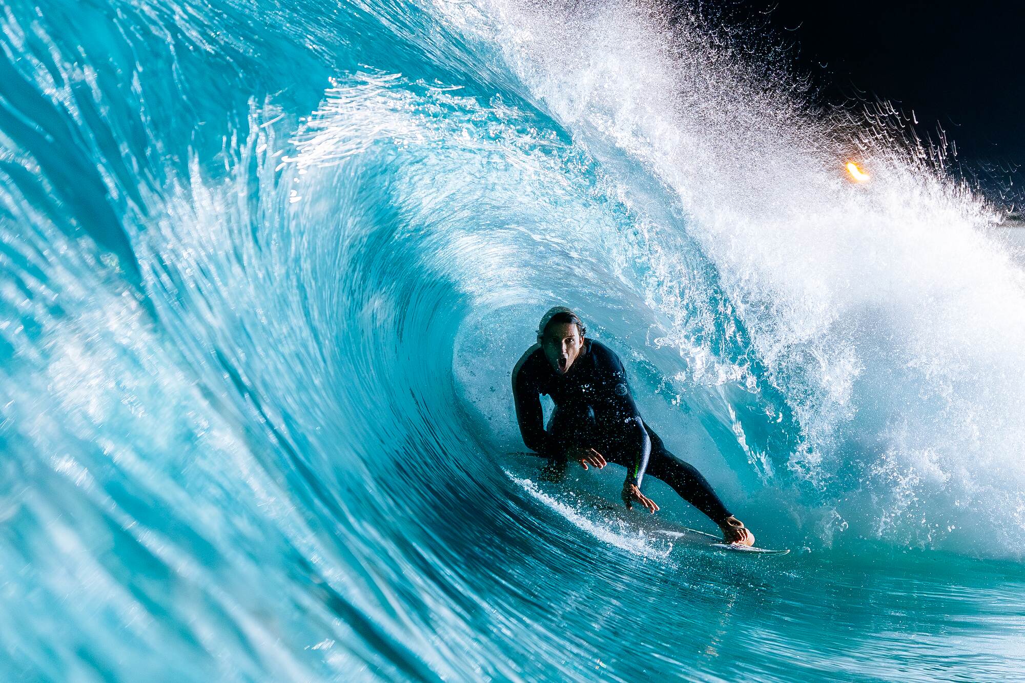 Surfer crouched inside a floodlit barrel at night