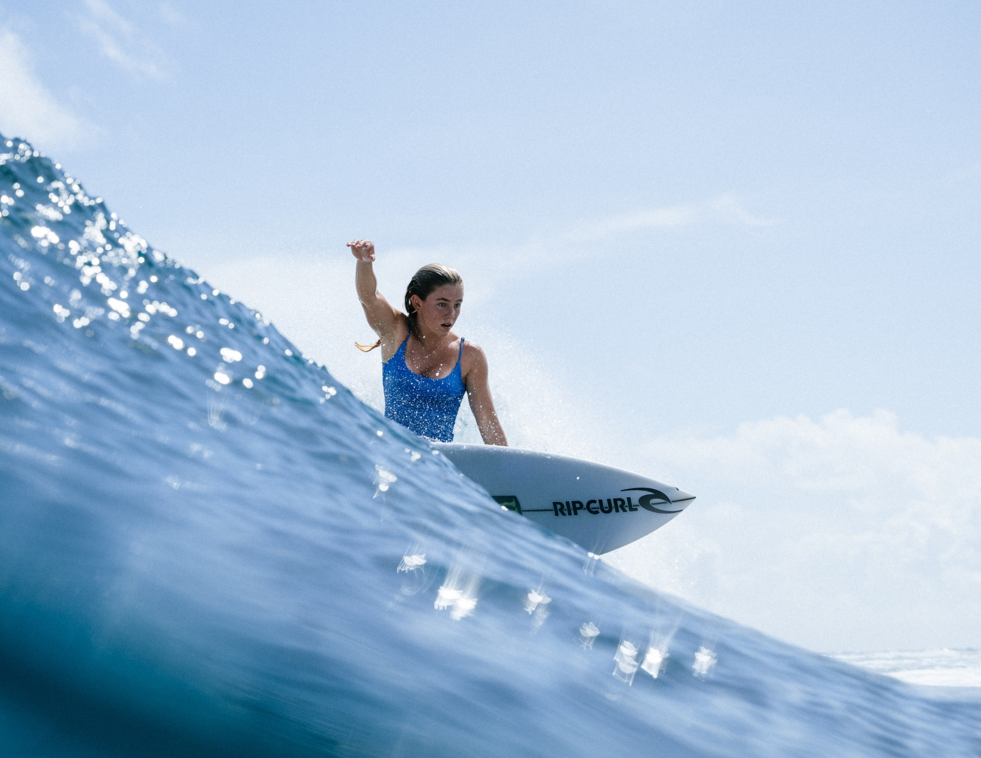 A surfer in a blue swimsuit drives a turn on a Rip Curl board, photographed from water level
