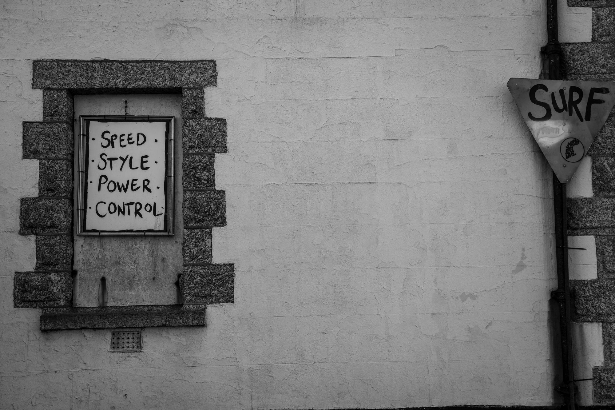 Black and white shot of a hand-painted sign reading Speed Style Power Control beside a surf sign