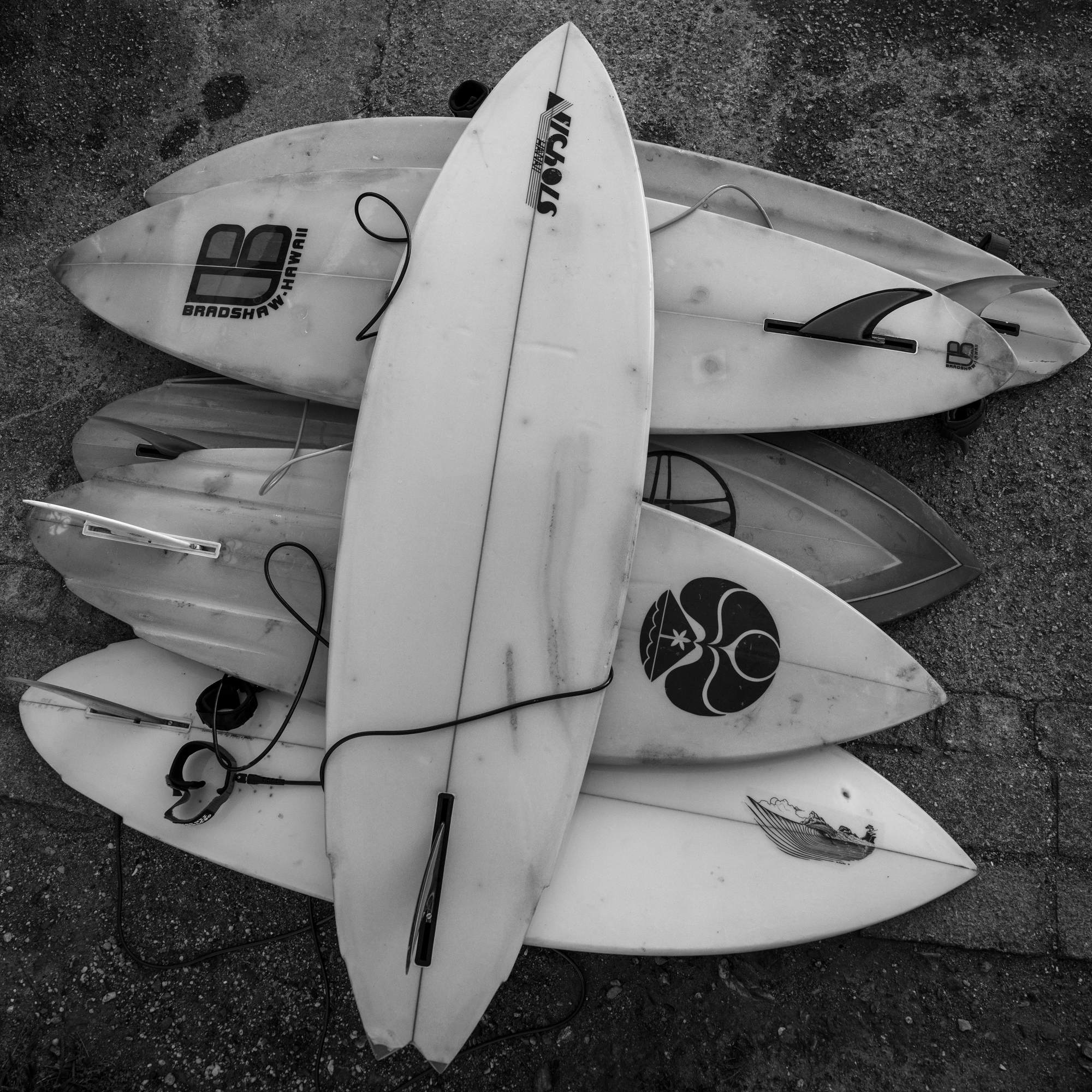 Black and white overhead shot of a stack of retro surfboards on concrete