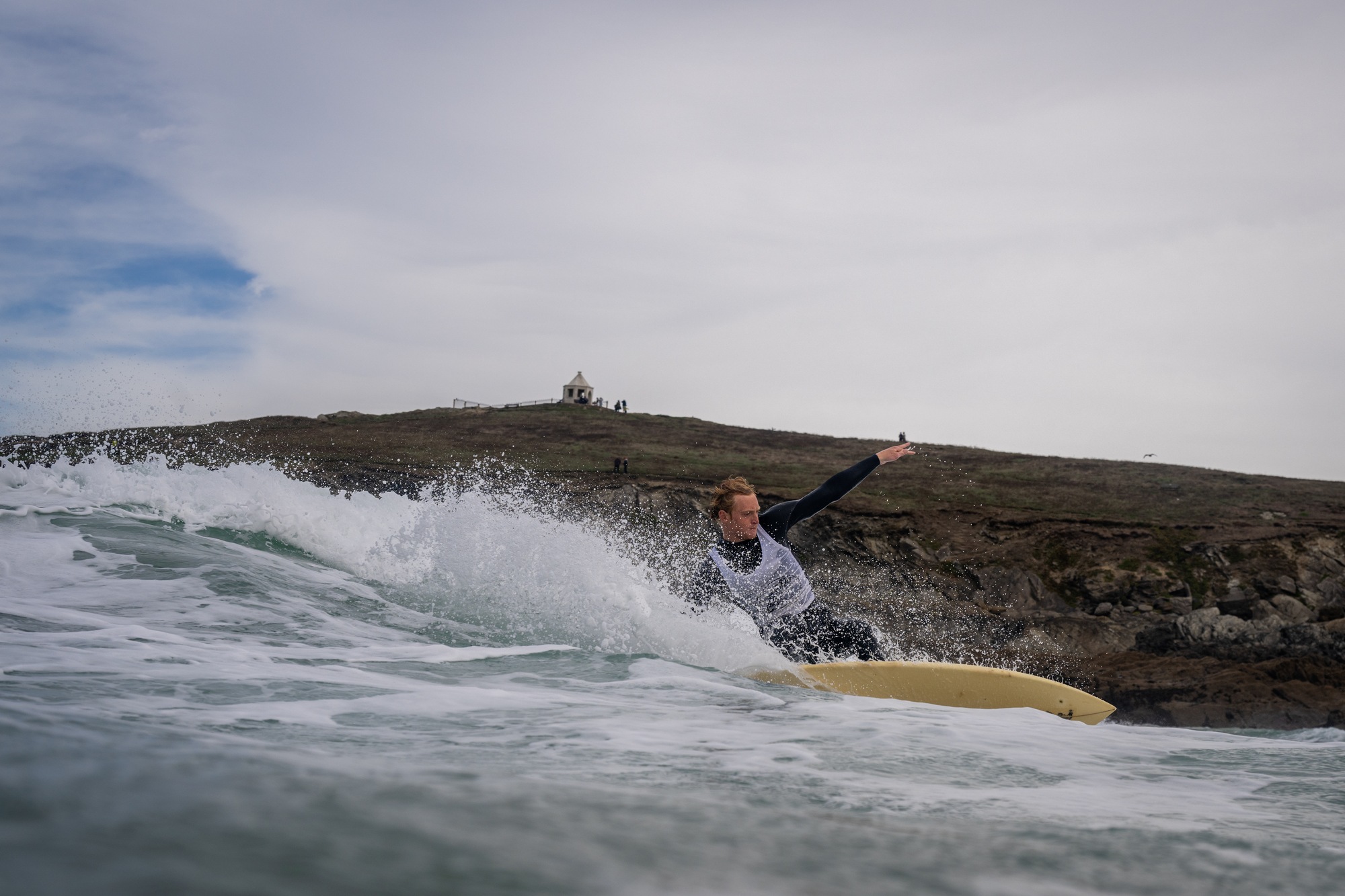 Surfer in a white bib cutting back on a cream single fin with a headland behind