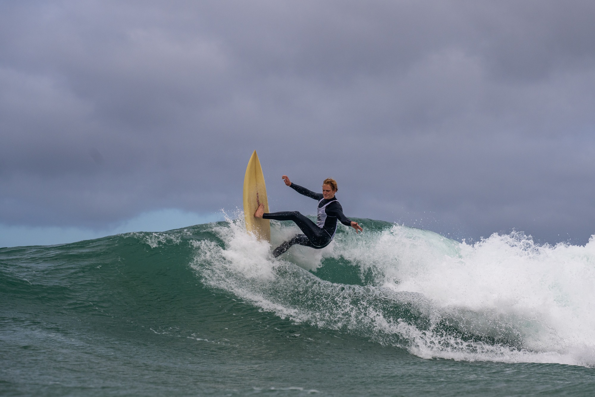 Surfer kicking the tail of a yellow single fin out under a stormy sky