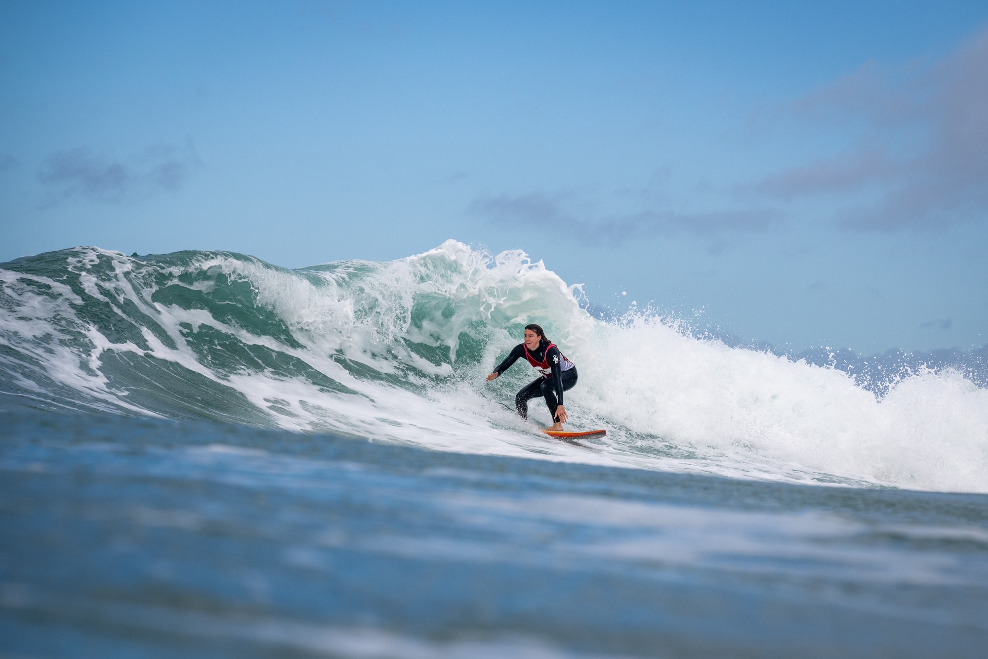 Surfer crouched low on a green wave under a blue sky